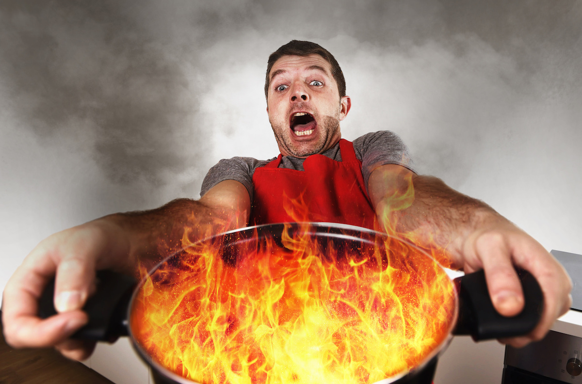 disaster home cook at kitchen- young funny and desperate man in cooking  apron holding pot in flames in stress and fear making a mess of fire and  smoke with food burning Stock